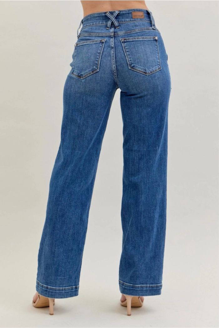 A person is shown from the back wearing High Waist Wide Leg Jeans and beige heels. The jeans have a wide-leg cut, large back pockets, and a crisscross belt detail. The setting features a plain, light-colored background.
