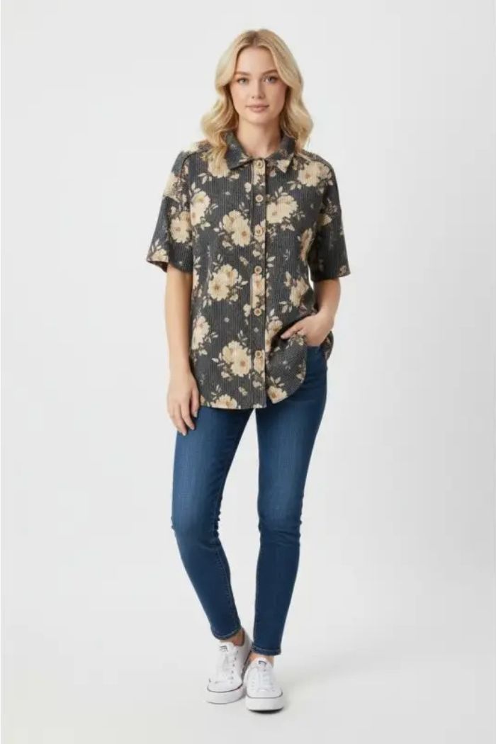 A woman stands against a plain background in the Floral Ribbed Button Top, blue skinny jeans, and white sneakers. With one hand in her pocket, she has a relaxed expression.