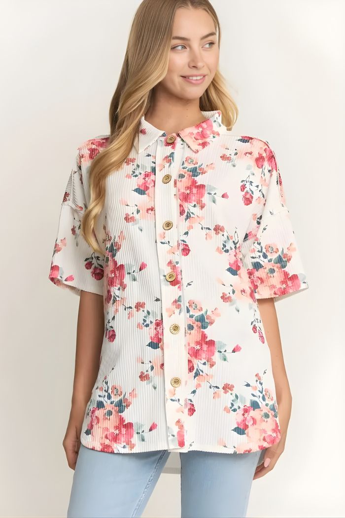 A woman stands against a light background wearing the Floral Short Sleeve Button Top, which features a loose fit and watercolor floral print in pastel tones, paired effortlessly with light blue jeans.