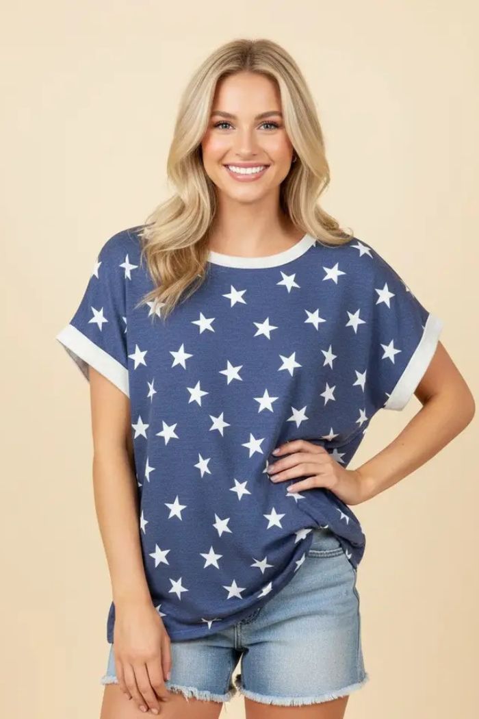 A smiling woman with long blonde hair wears the Plus Star Terry Top, featuring a blue star print and white trim, paired with light denim shorts as she stands against a beige background.