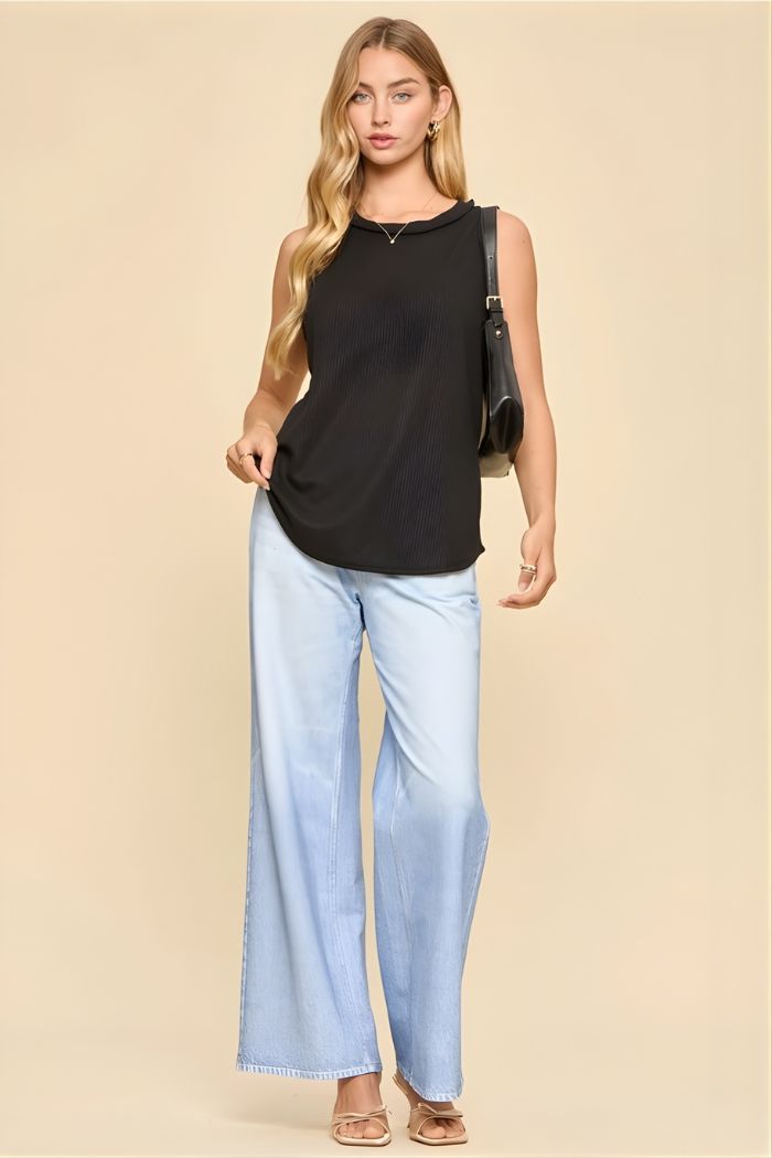A woman with long, wavy blonde hair stands against a beige background wearing the Basic Knit Tank Top, light blue wide-leg jeans, nude open-toe heels, and carrying a black shoulder bag.