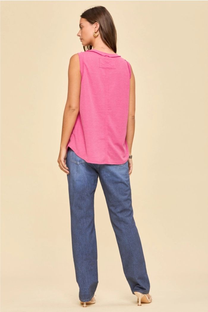 A woman faces away, wearing the Basic Knit Tank Top in pink, blue jeans, and beige heels against a plain beige background.