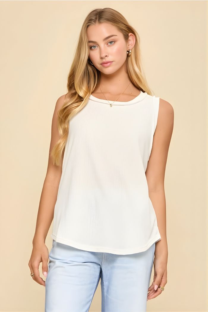 A young woman with long blonde hair wears the Basic Knit Tank Top and light blue jeans, standing against a beige background and looking at the camera with a neutral expression.