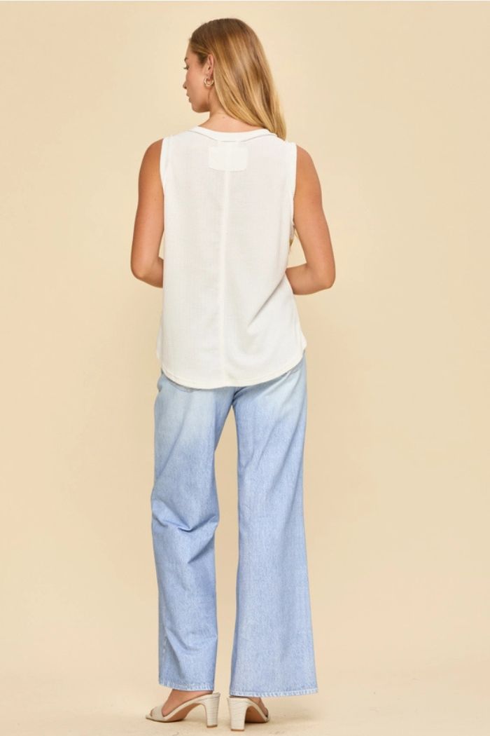 A woman with long blonde hair faces away, wearing the Basic Knit Tank Top, light blue wide-leg jeans, and white heeled sandals against a beige background.