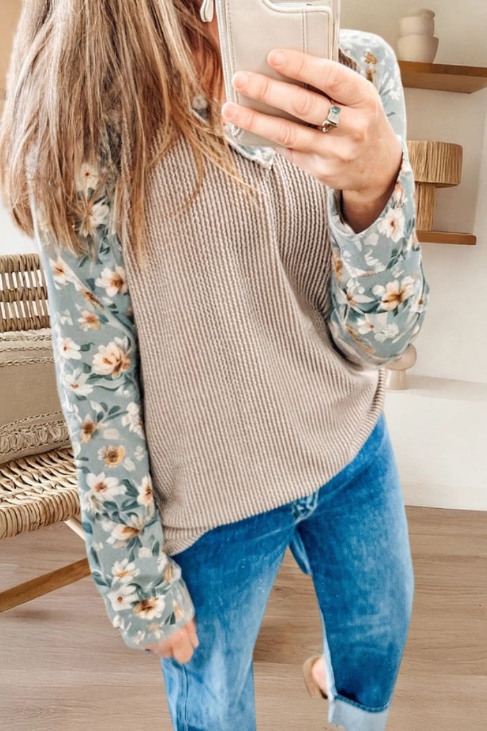 A person taking a mirror selfie wears the Floral Contrast Ribbed Top with a beige knit vest and blue jeans. Their face is partially out of frame as they hold up their phone.