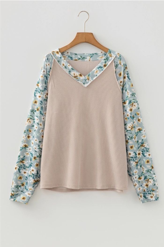 The Floral Contrast Ribbed Top showcases a beige ribbed body, blue floral-patterned sleeves, and a matching V-neck trim, displayed on a wooden hanger against a white background.