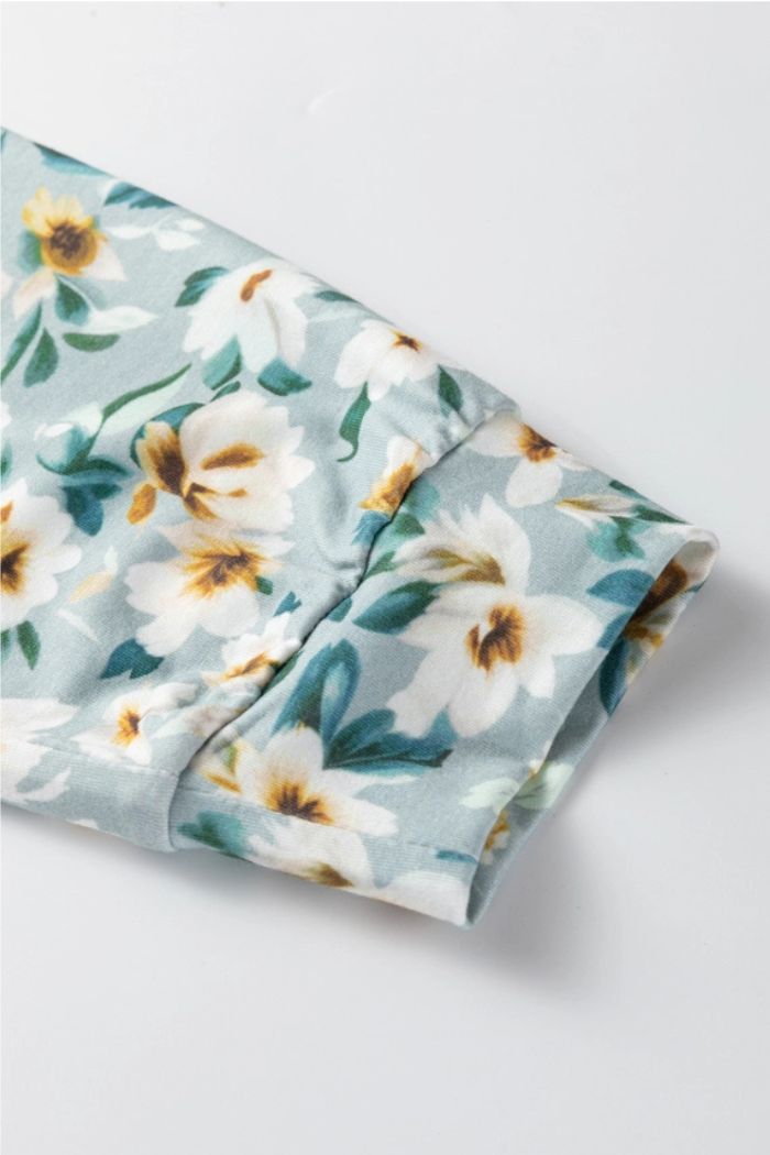 A close-up of the Floral Contrast Ribbed Top against a soft blue background, highlighting its white and yellow floral pattern with green leaves and showcasing its smooth, lightweight ribbed fabric.
