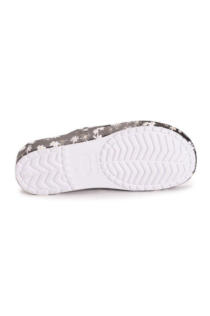 The image features the sole of Black Floral Slip-On Sandals with a white, textured zigzag tread. The sides display a black background adorned with white and light-colored floral patterns.