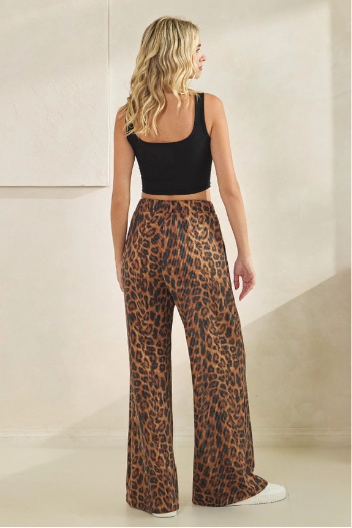 A woman with wavy blonde hair, seen from behind, wears a black sleeveless crop top and Leopard Ribbed Lounge Pants in a neutral indoor setting.