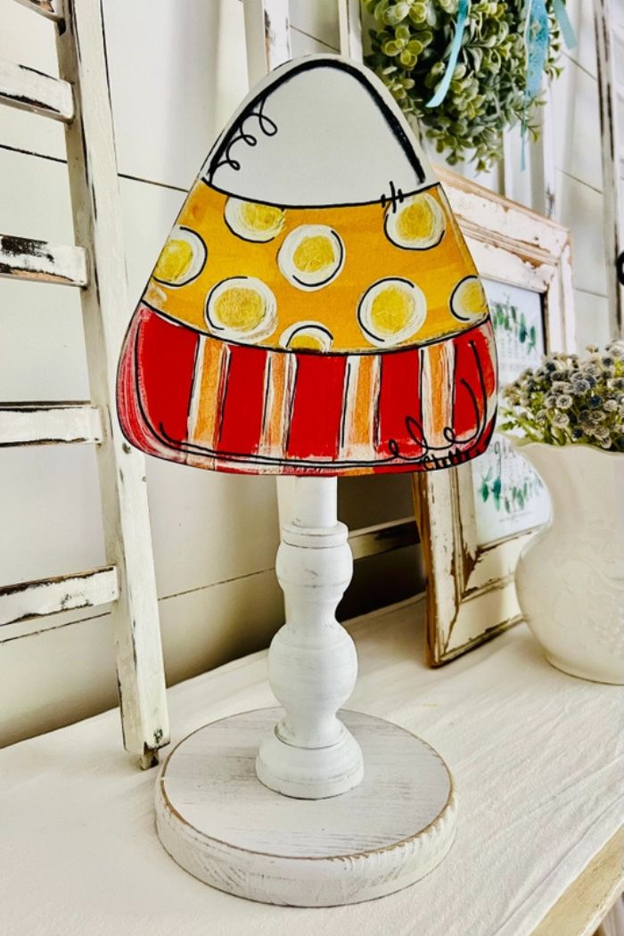 Add a charming touch to your autumn decor with Fall Wood Toppers—a hand-painted candy corn featuring yellow dots and red stripes on a white pedestal. Perfect for farmhouse seasonal displays, it looks great on any surface with rustic accents.