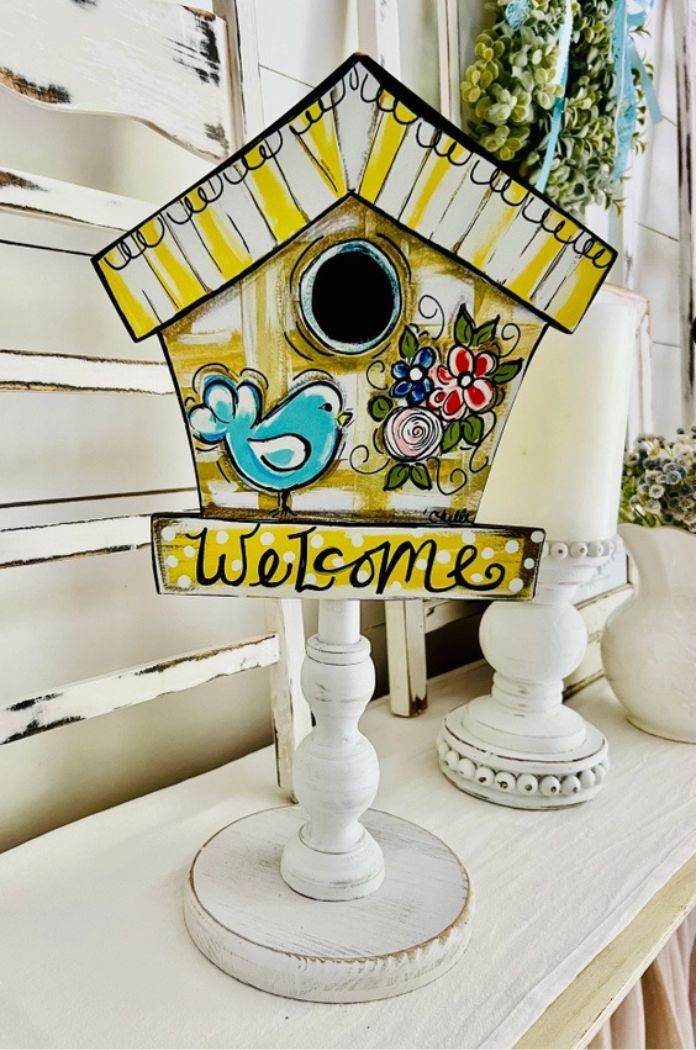 The Spring Summer Wood Toppers, featuring yellow stripes, a blue bird, flowers, and "Welcome" on a white pedestal, add charming seasonal décor to any bright shabby-chic room.