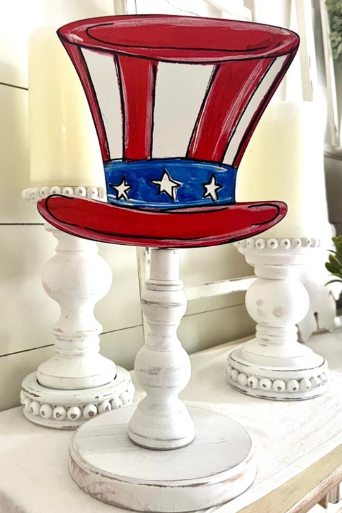 The Spring Summer Wood Toppers feature a decorative Uncle Sam hat cutout in red, white, and blue with stars on a wooden stand—perfect for home décor or seasonal displays alongside white candle holders on any surface.