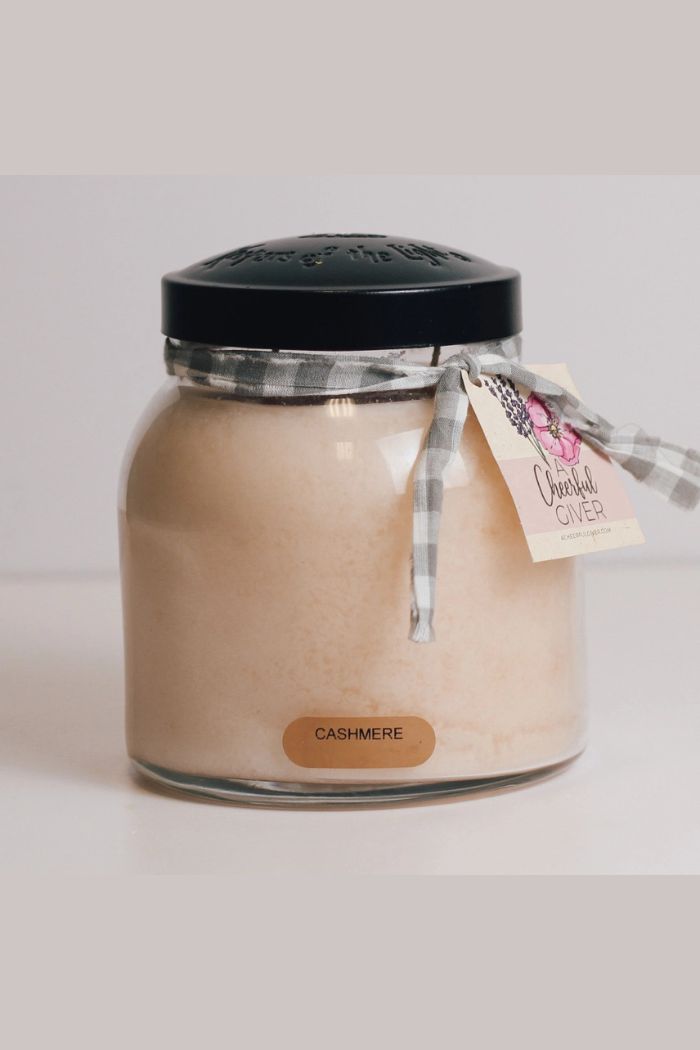 The Papa 34oz Candle is a large beige Cashmere-scented candle in a glass jar with a black lid and gray gingham ribbon tag reading Cheerful Giver, creating a decorative accent against a plain, light background.