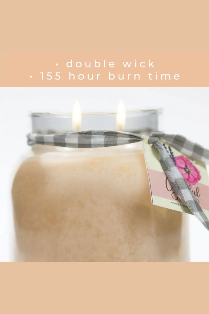 The Papa 34oz Candle features two lit wicks, a gray plaid ribbon, and a floral tag. Text above reads: double wick • 155 hour burn time on a peach background—a stylish large candle for any space.