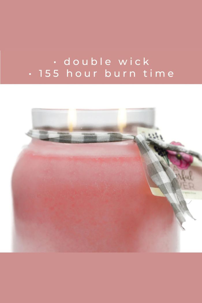 The Papa 34oz Candle is a pink decorative jar with two lit wicks and a plaid ribbon tied around the top. “Double wick • 155 hour burn time” appears above on a matching pink background.