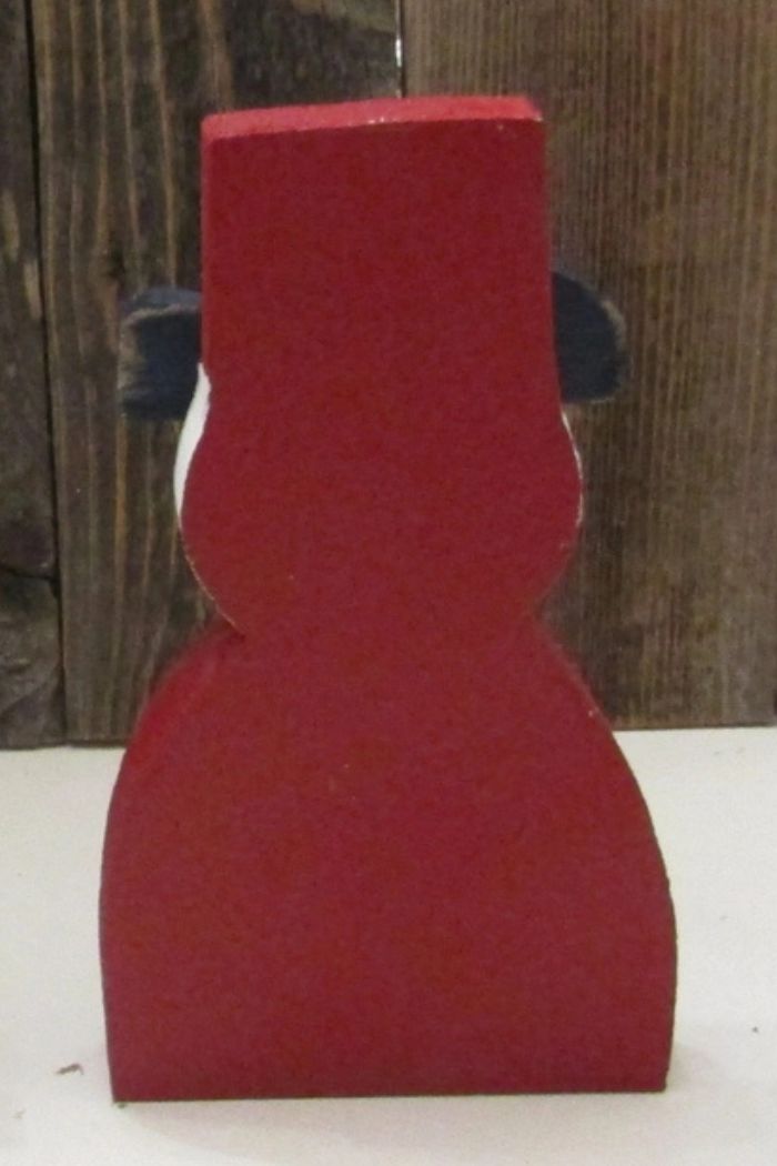 The Patriotic Uncle Sam Decor, a red-painted wooden figure, stands on a white surface with a rustic wood background and is shown from the back—a unique Americana accent for your home.