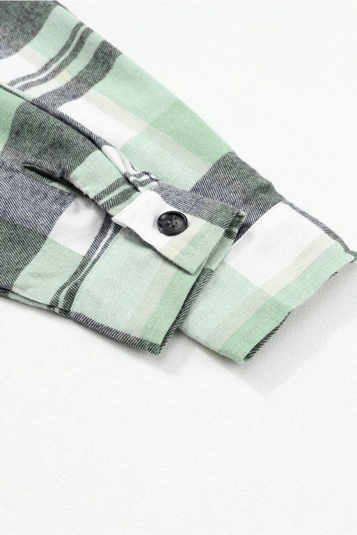 Close-up of the Plaid Button Up Shirt sleeve in green, white, and black plaid with a single black cuff button, laid flat on a white background.