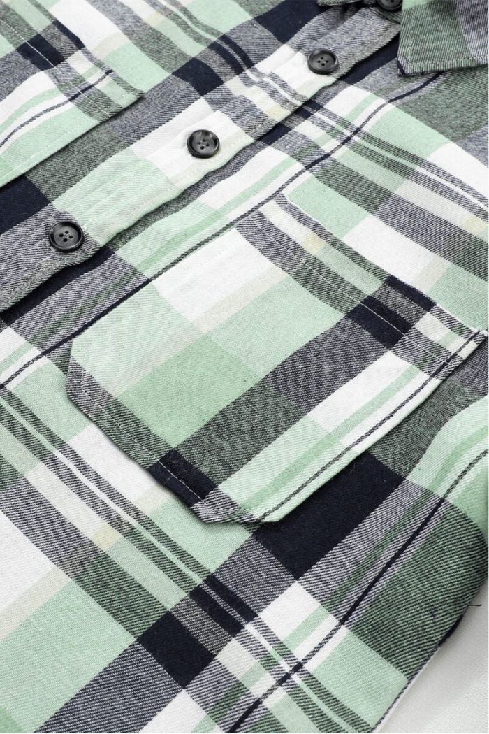 Close-up of a Plaid Button Up Shirt in green, black, and white with buttons, chest pocket, and collar detail. This long sleeve shirt features a soft woven flannel texture.