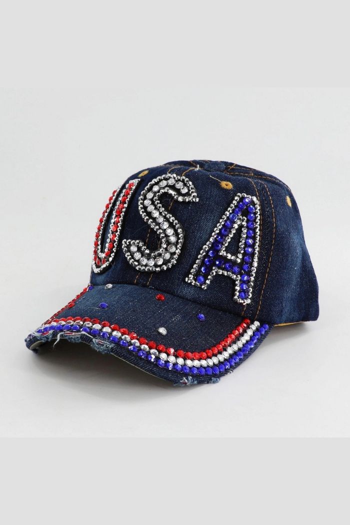 The USA Crystal Baseball Cap features denim fabric, sparkling "USA" rhinestone beads on the front, and red, white, and blue brim accents. Displayed against a plain background.