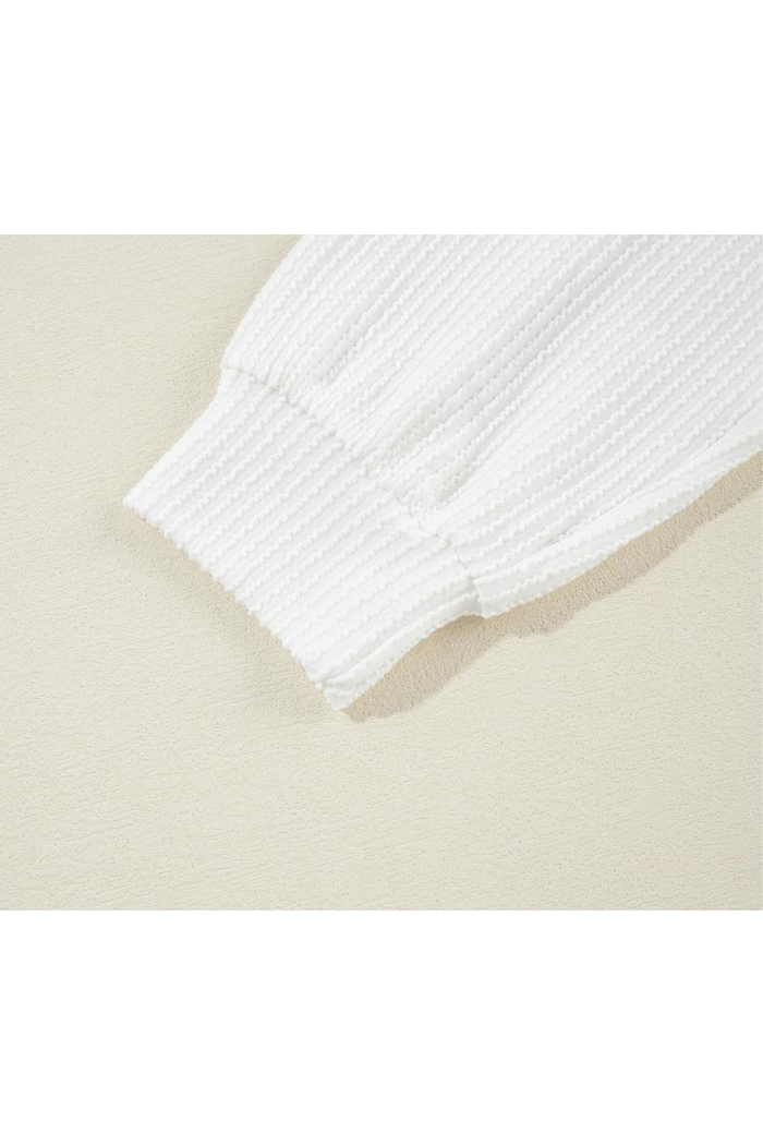 Close-up of the ribbed cuff sleeve from the USA Flag Graphic Sweatshirt, featuring white textured fabric, laid flat on a light beige surface.