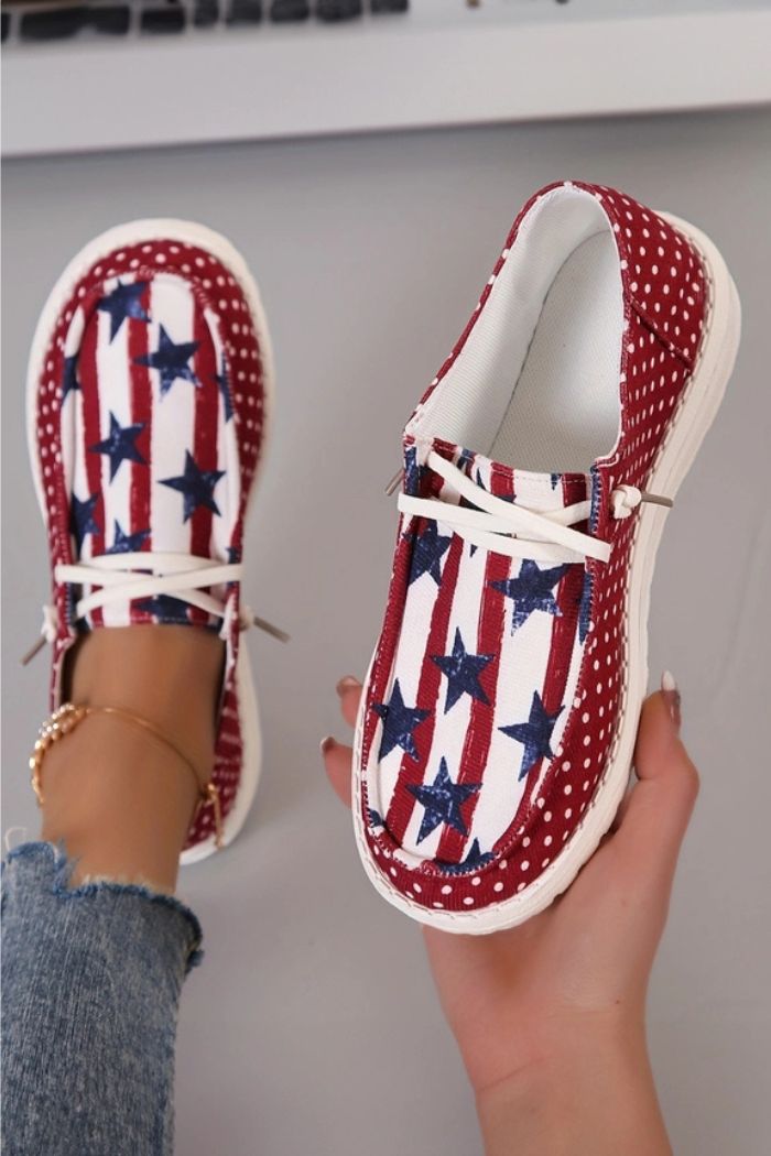 A person wears Americana Mash Print Sneakers—canvas slip-ons with a red, white, and blue stars-and-stripes print and red polka dot trim—paired with blue jeans and an anklet.