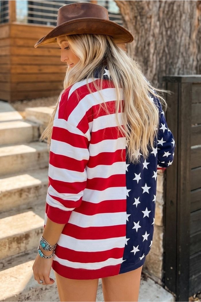 A woman in a brown hat and USA Flag Quarter Zip stands outdoors with her back to the camera. Steps, a large tree, and a wooden fence are visible in the background.