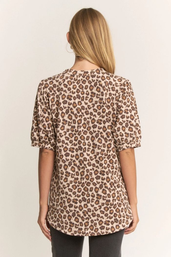 A woman with long blonde hair is seen from behind wearing the Animal Ribbed Puff Top, an oversized animal print piece with short sleeves, paired with dark pants against a plain light background.