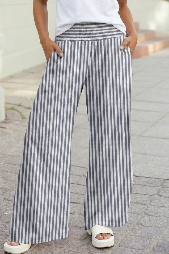 Someone stands on a paved sidewalk with hands in pockets, wearing Striped Wide Leg Pants—loose, high waisted, gray and white striped—paired with a white top and white platform sandals.