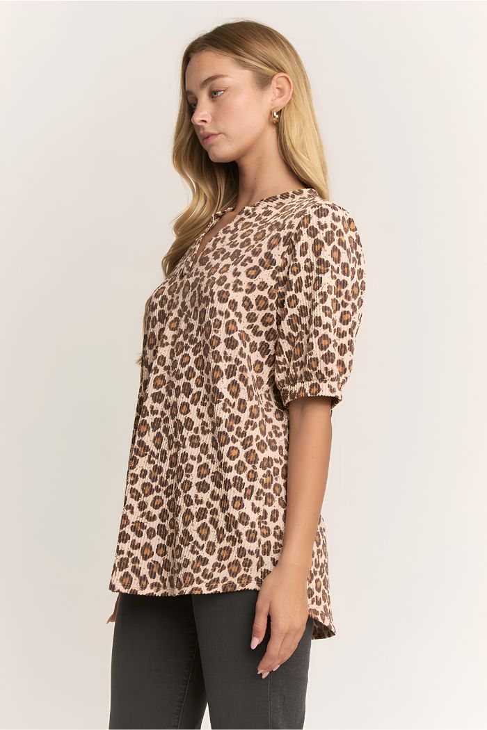 A woman with long blonde hair, wearing a Plus Animal Ribbed Top and dark pants, stands in profile against a plain light background.