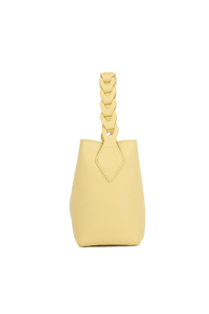 A side view of the Lorna Crossbody Bag, a small light yellow bag with textured faux leather, a braided handle, and a compact structured shape, displayed against a white background.