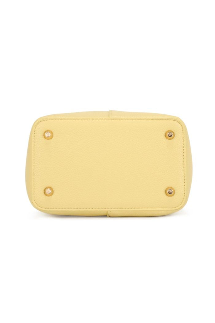 The Lorna Crossbody Bag is a rectangular, light yellow faux leather bag shown from the bottom, with a compact structured shape and four metal feet at each corner.