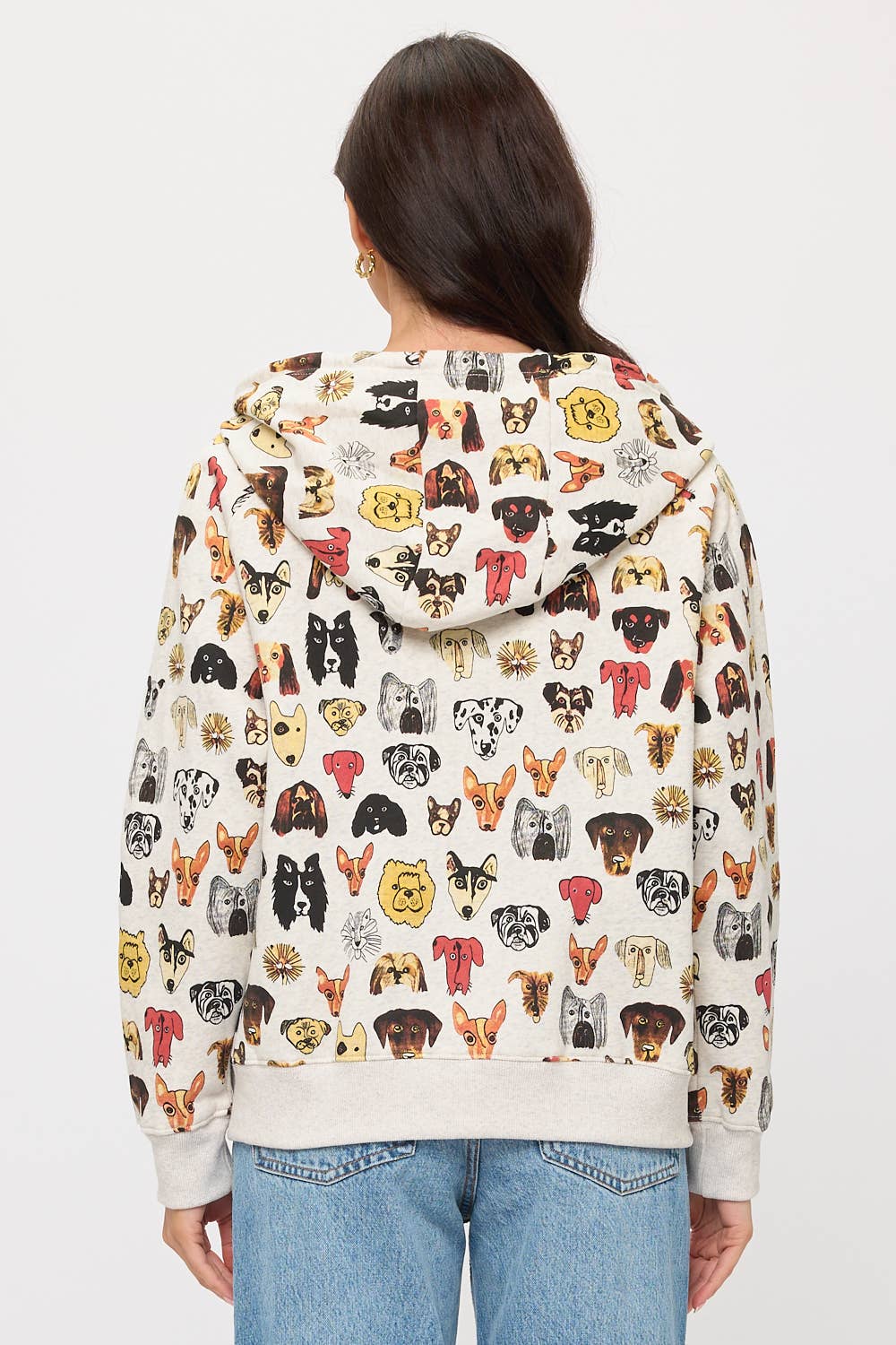 A person in blue jeans stands with their back to the camera, wearing the COLORFUL DOG FACES PRINT ZIP UP HOODIE—a vibrant choice of apparel for dog lovers.
