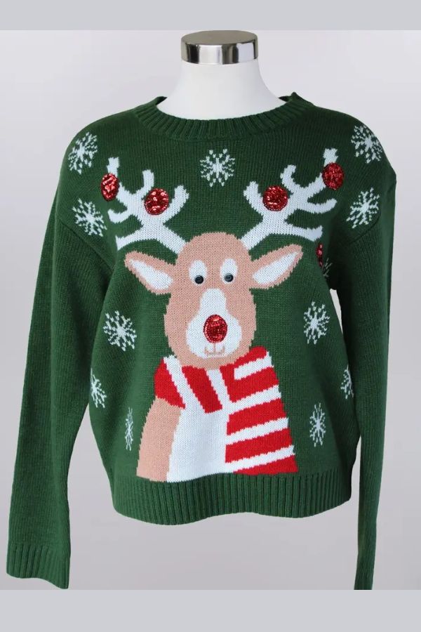 The Sequin Reindeer Christmas Sweater is green and showcases a festive reindeer with antlers, red ornaments, white snowflakes, and a red and white striped scarf. The reindeer’s red nose adds a playful touch to the standout holiday design.