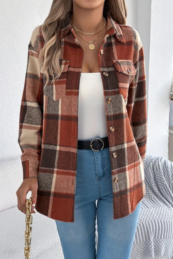 A woman wearing the Rust Plaid Longline Coat over a white top and blue jeans, accessorized with layered gold necklaces and a gold chain purse. Her loose, wavy hair complements the outfit—an ideal lightweight layering piece for cool days.