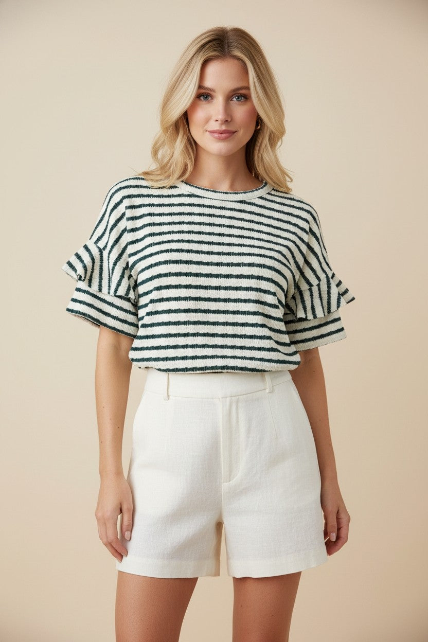 A woman with blonde hair wears the Stripe Ruffle Sleeve Top and high-waisted white shorts, standing against a plain beige background and smiling slightly.