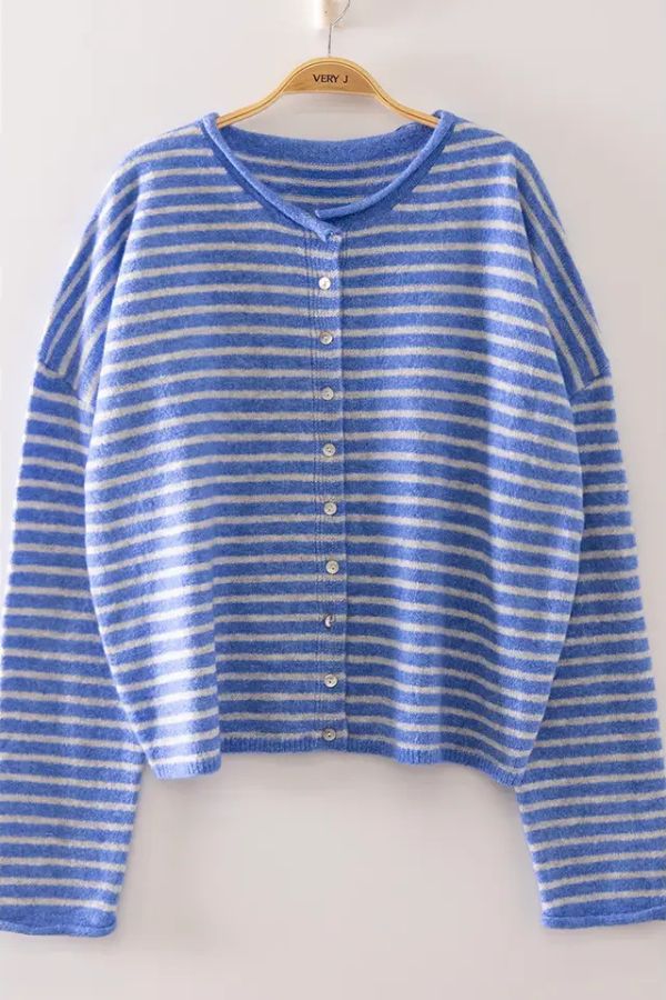 The Striped Button Front Sweater is a cozy knit cardigan in blue and white horizontal stripes, featuring long sleeves and classic white buttons. Designed for women, this button-front sweater hangs elegantly on a wooden hanger against a light background.