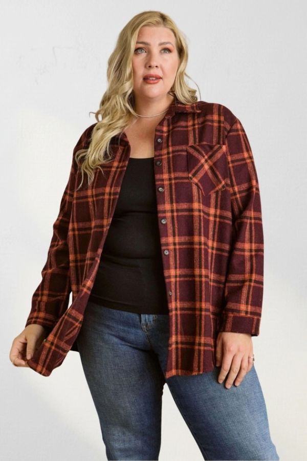 A person wearing a Curvy Plaid Flannel Shirt in maroon and orange, unbuttoned over a black tank top and blue jeans.