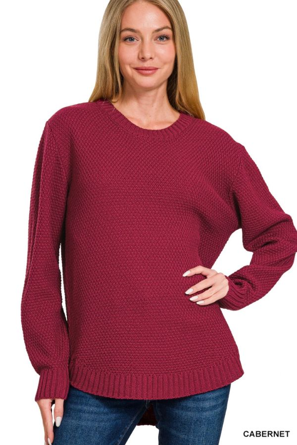 A woman wearing the Everyday Crew Neck Sweater, featuring a textured knit and long sleeves in a rich wine color, pairs it with blue jeans as she stands with one hand on her hip, smiling at the camera.