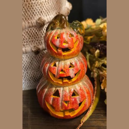 The LED Jack-O’-Lantern Stack features three vibrant orange pumpkins with carved faces and green tops, displayed next to a textured white object and dried flowers. Crafted to resemble ceramic, this festive accent makes the perfect LED pumpkin décor piece for your home during Halloween.