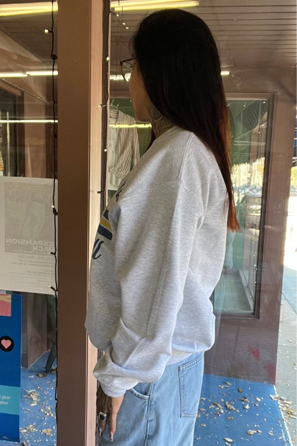 Side view of a person wearing a light grey Milwaukee Baseball Crewneck Sweatshirt with a graphic design featuring blue and yellow lettering across the chest.