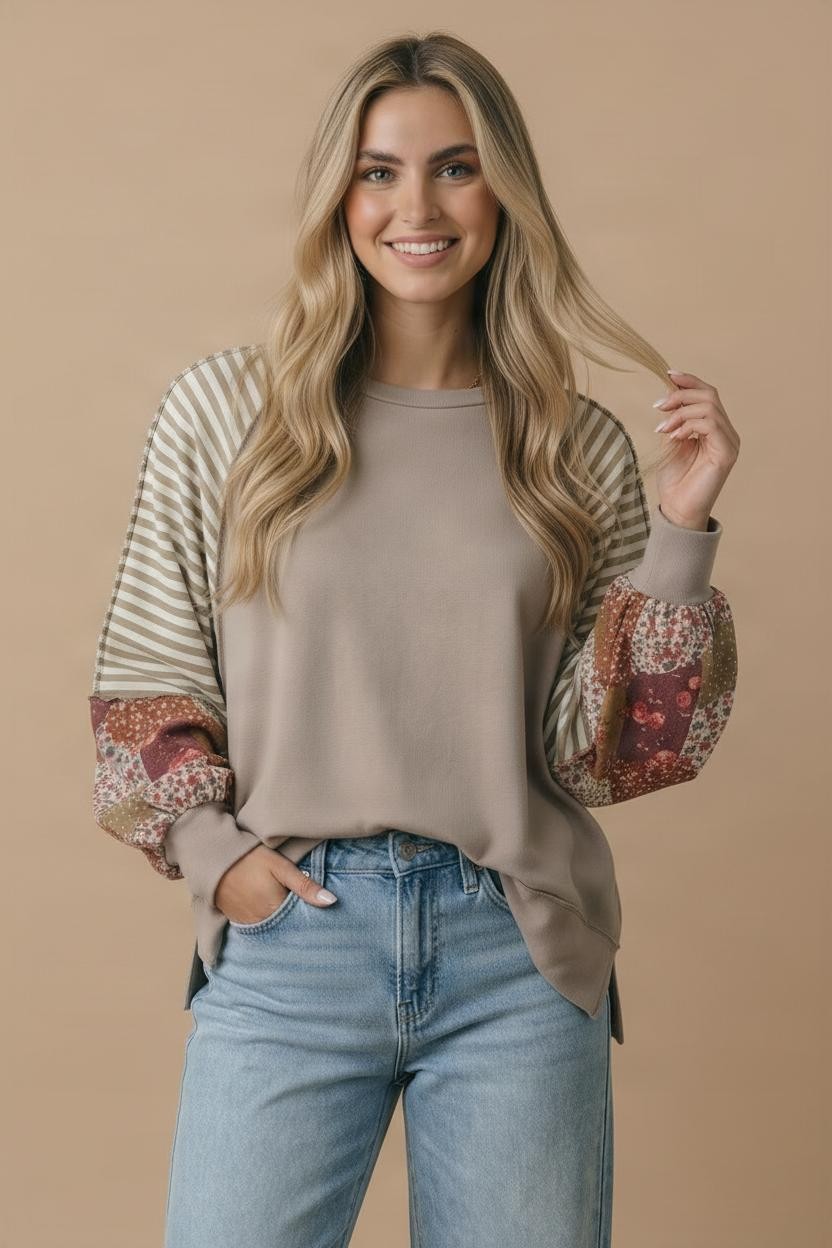 A woman with long blonde hair smiles while wearing the Plus Patchwork Sleeve Top and light blue jeans, standing against a tan background with one hand in her pocket.