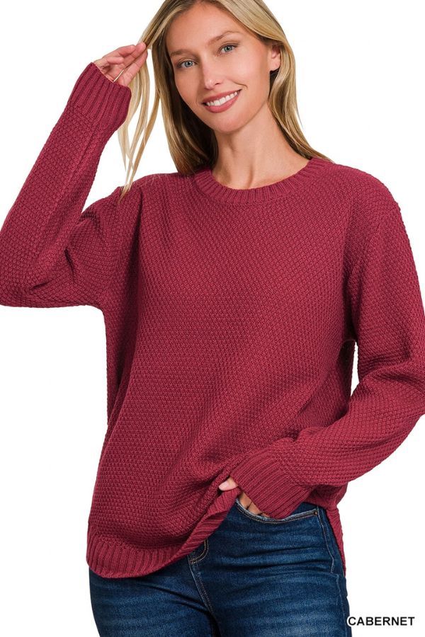A woman smiles and poses against a white background, wearing the Everyday Crew Neck Sweater—a textured knit, long-sleeve sweater in dark red—paired with blue jeans.
