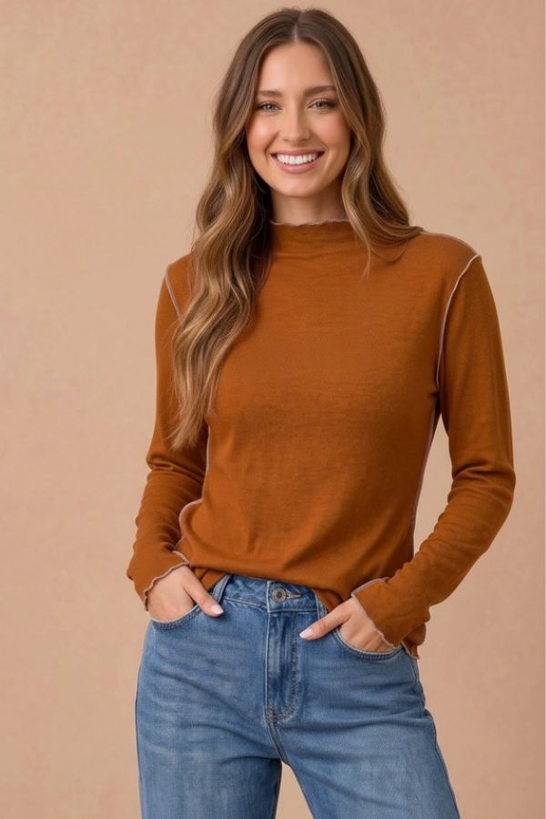A woman wearing a rust-colored Frilled Mock Neck Hacci Top featuring a lightweight knit, mock neck, lettuce-edge trim, and exposed seam detailing.