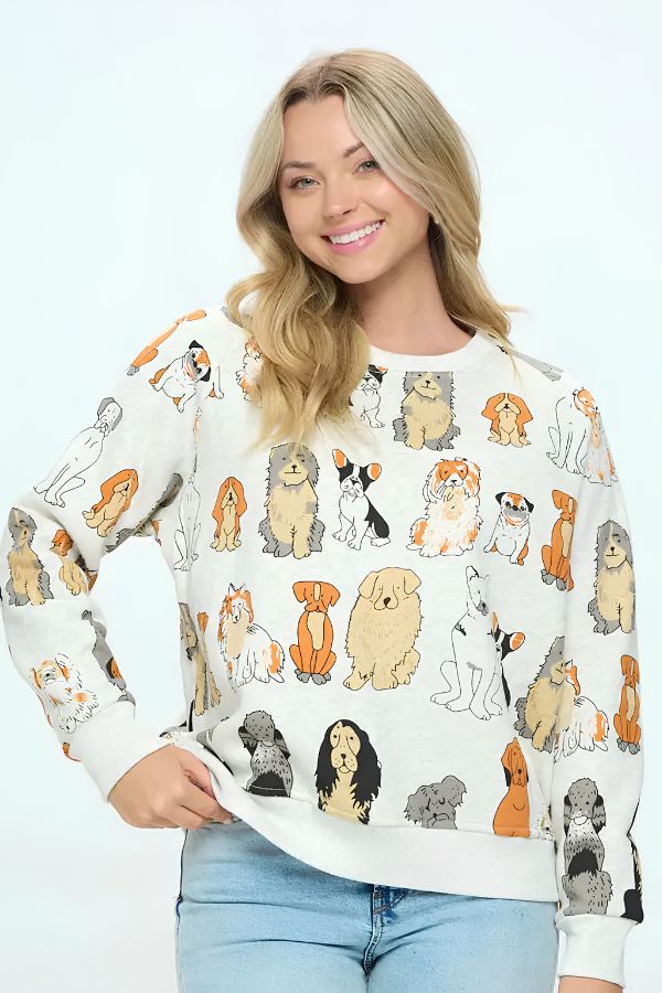 A smiling woman models the Dog Print Crewneck Sweatshirt, featuring colorful cartoon dog illustrations, styled with light blue jeans and one hand on her hip against a plain light background—an ideal choice for dog lovers.