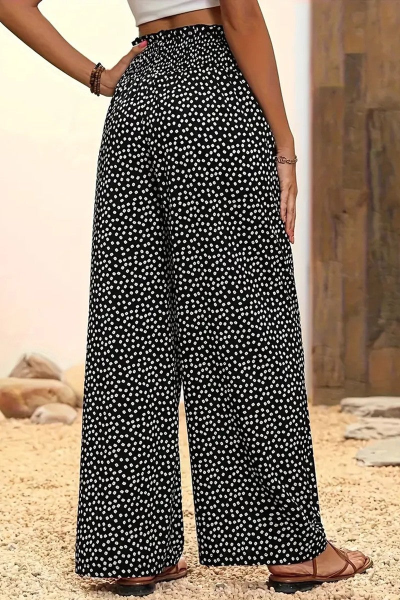 A person stands indoors on a light gravel surface, wearing the Polka Dot Wide Leg Pants with an elastic waistband, paired with a cropped white top, sandals, and bracelets.