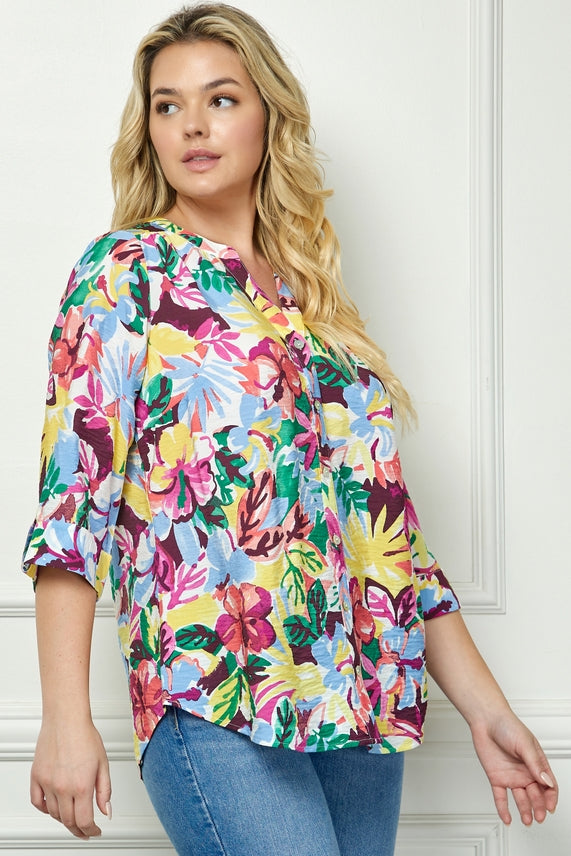 A woman with long blonde hair wears the Plus Floral Placket Blouse and blue jeans, standing against a white paneled wall and looking to the side.