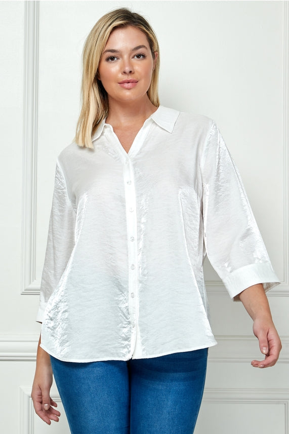 A woman with blonde hair wears the Plus Shimmer Collar Blouse, an oversized white top with a shimmery finish and three-quarter sleeves, paired with blue jeans as she stands in front of a white wall.