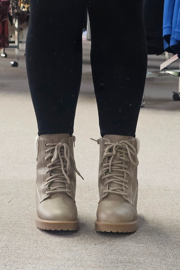 Person wearing black leggings and tan Sky Solange Wedge Boots stands on a beige carpeted floor, with clothing racks visible in the background.