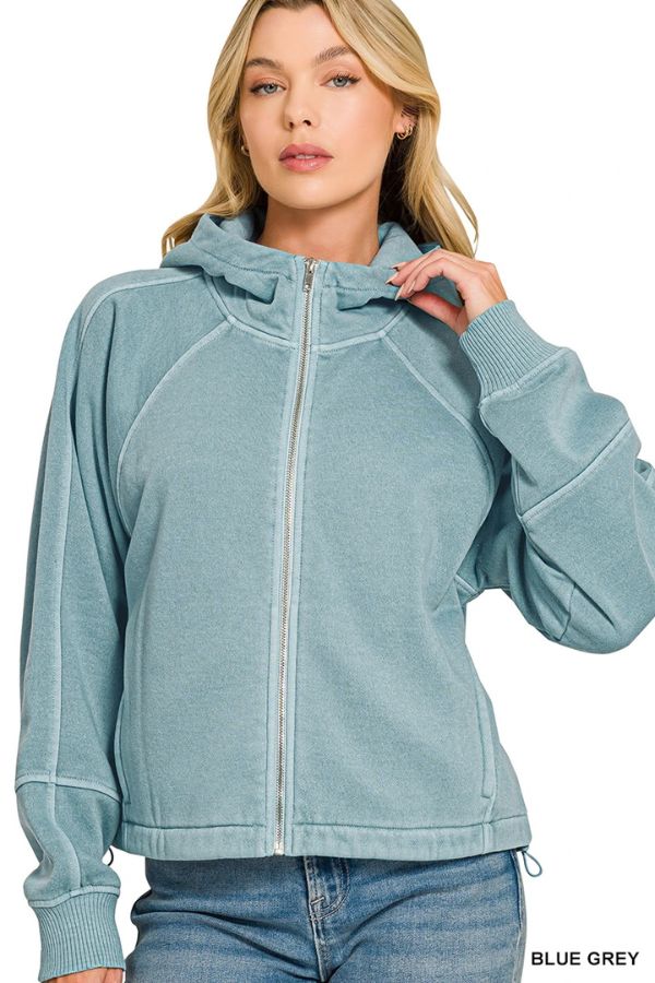 A woman in the Pigment Dye Zip Up Hoodie with a relaxed fit, blue-grey color, touching the collar and wearing blue jeans.