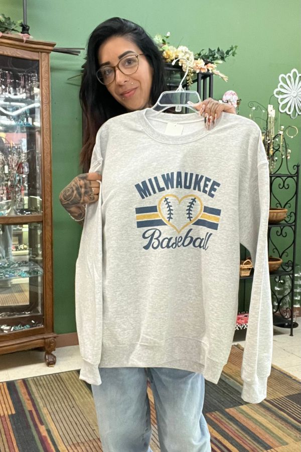 A person holds up a grey Milwaukee Baseball Crewneck Sweatshirt featuring a baseball heart graphic.